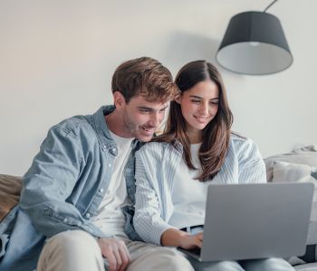 Junges Paar auf einer Couch recherchiert im Internet nach PKV